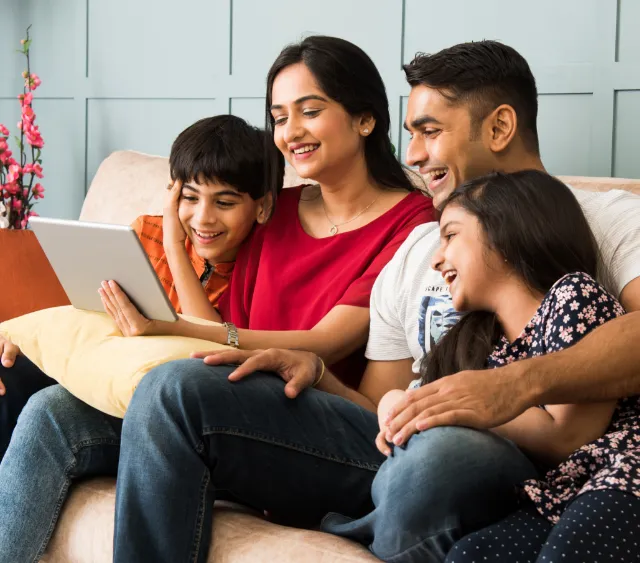 Family of four on a couch looking at a tablet screen together